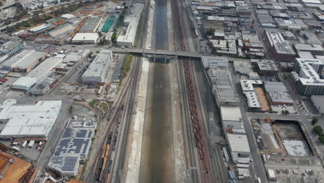 AERIAL:-Los-Angeles-River-with-Water-Tilt-up-revealing-Highway-and-LA-Cityscape-on-Cloudy-Overcast-Sky